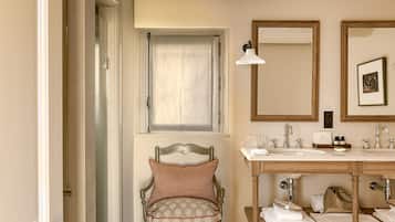 Une salle de bain avec un meuble-lavabo en bois, une chaise avec un coussin, un miroir et une fenêtre avec un rideau.