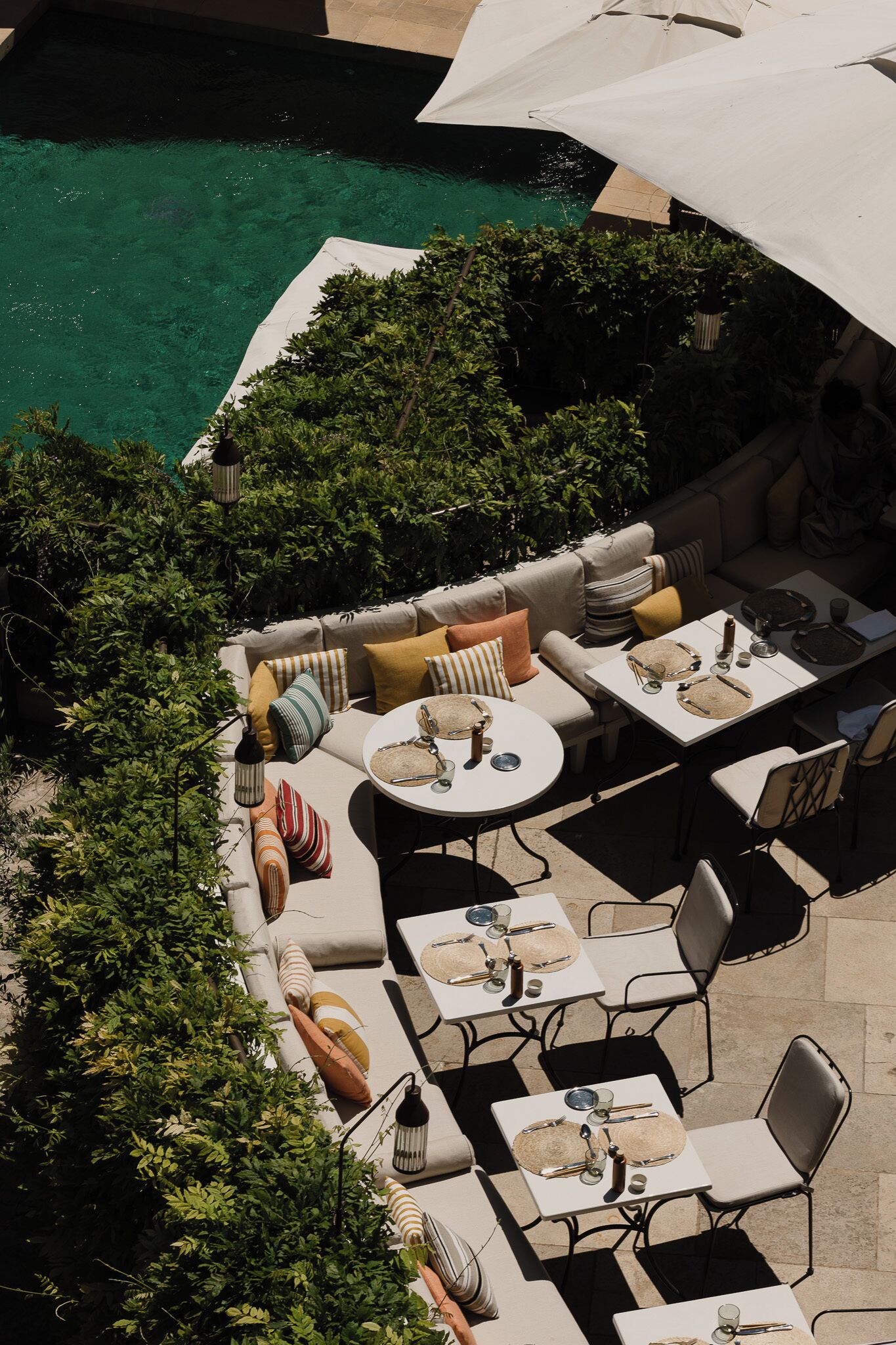 An outdoor patio with seating and tables, surrounded by lush greenery and a pool.