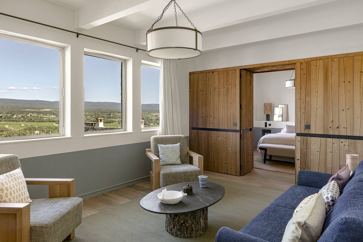 Een moderne kamer met een groot raam, een ronde houten tafel, een bank en een houten garderobe.