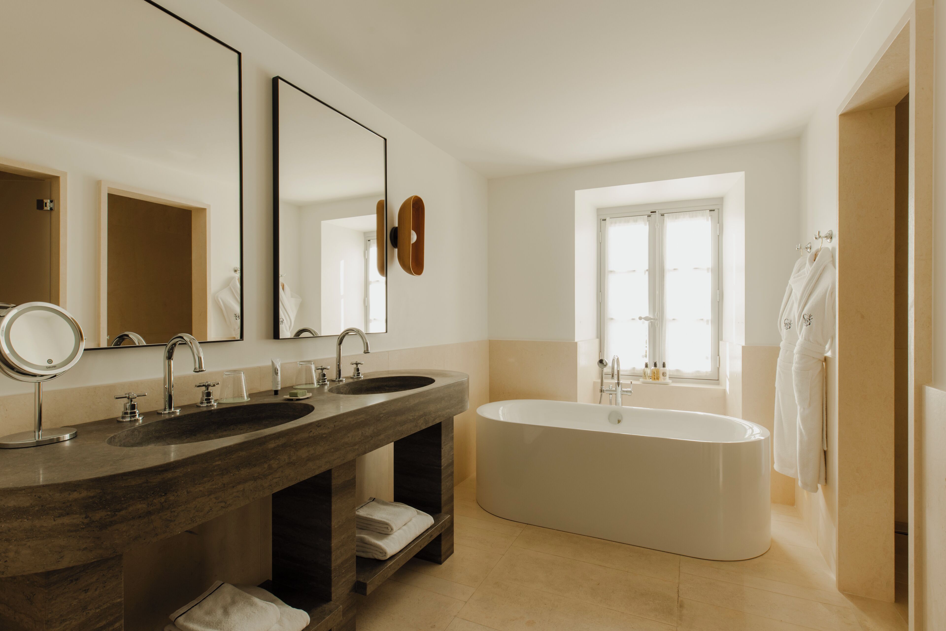 A modern bathroom with two sinks, a large bathtub, and a window providing natural light.