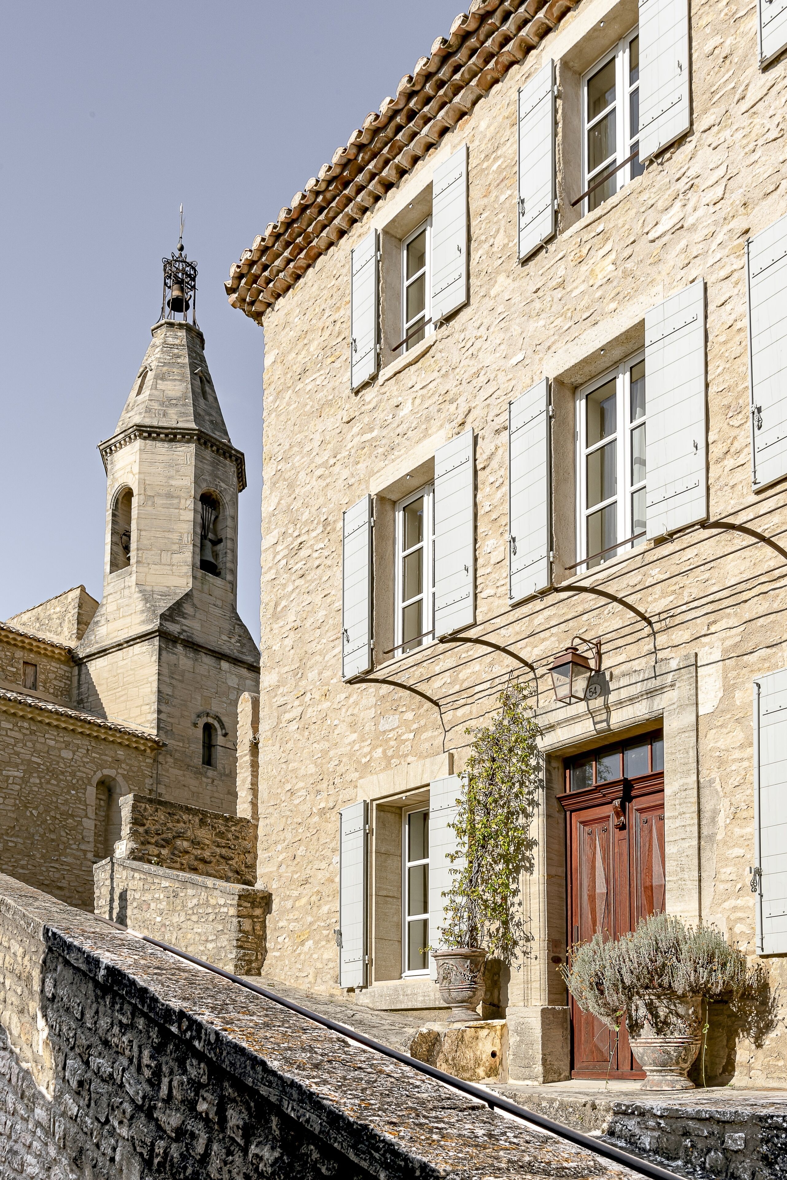 A stone building with a bell tower, a wooden door, and a potted plant.