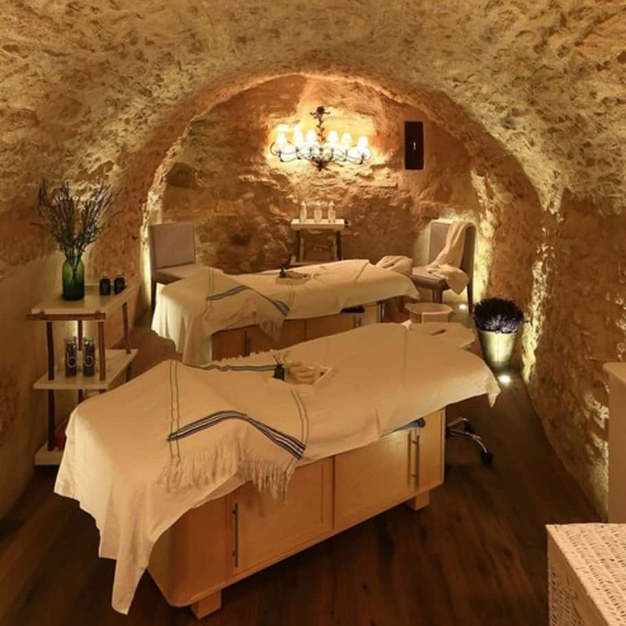 A cozy, stone-walled room with two wooden beds, a small table, and a chandelier.