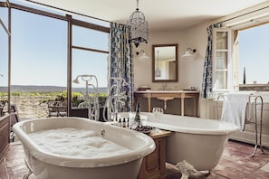 A bathroom with two freestanding tubs, a large window with a view of the beach, and a hanging light fixture.
