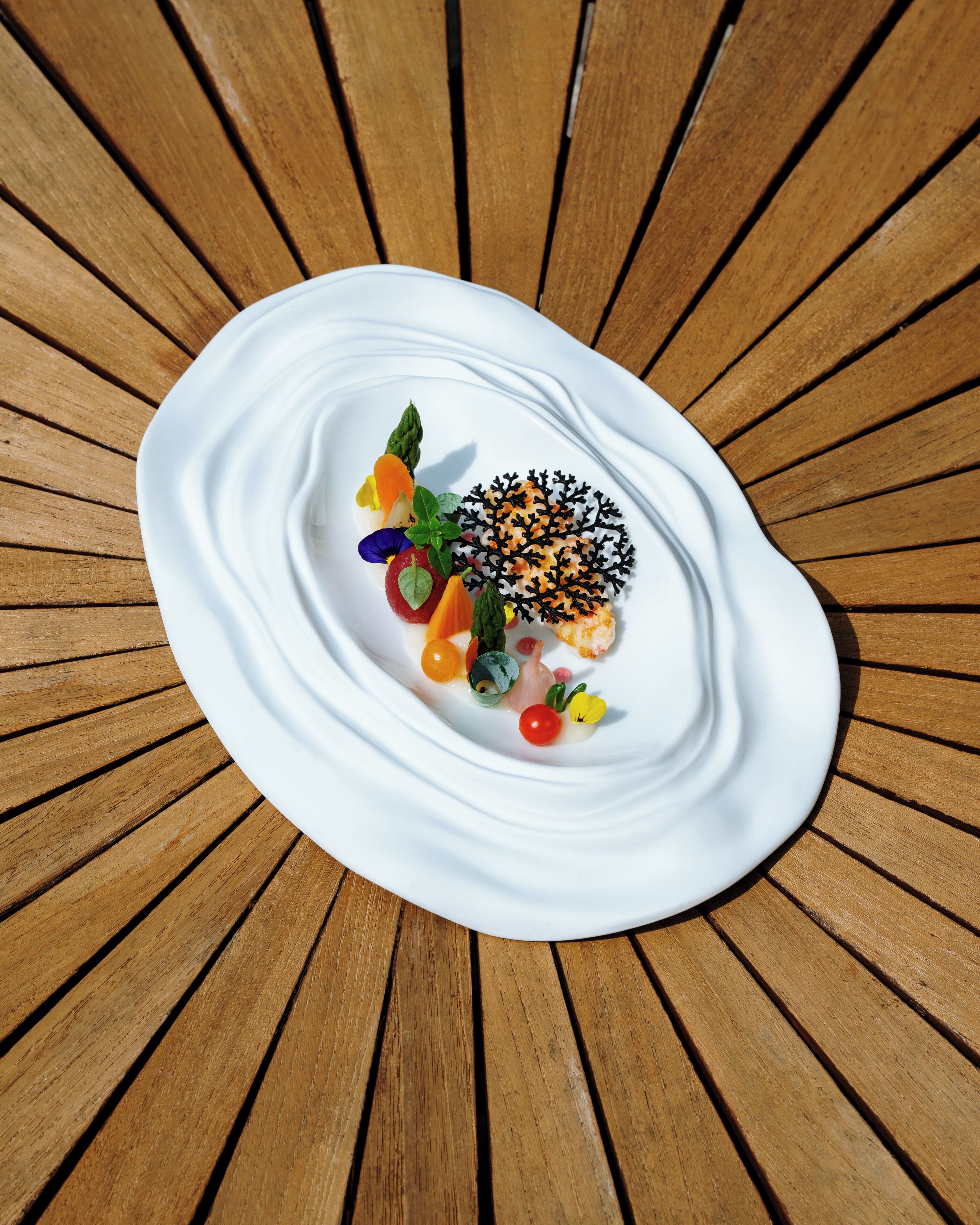 A white plate with a variety of colorful food items and a decorative black leaf-like garnish on a wooden table.