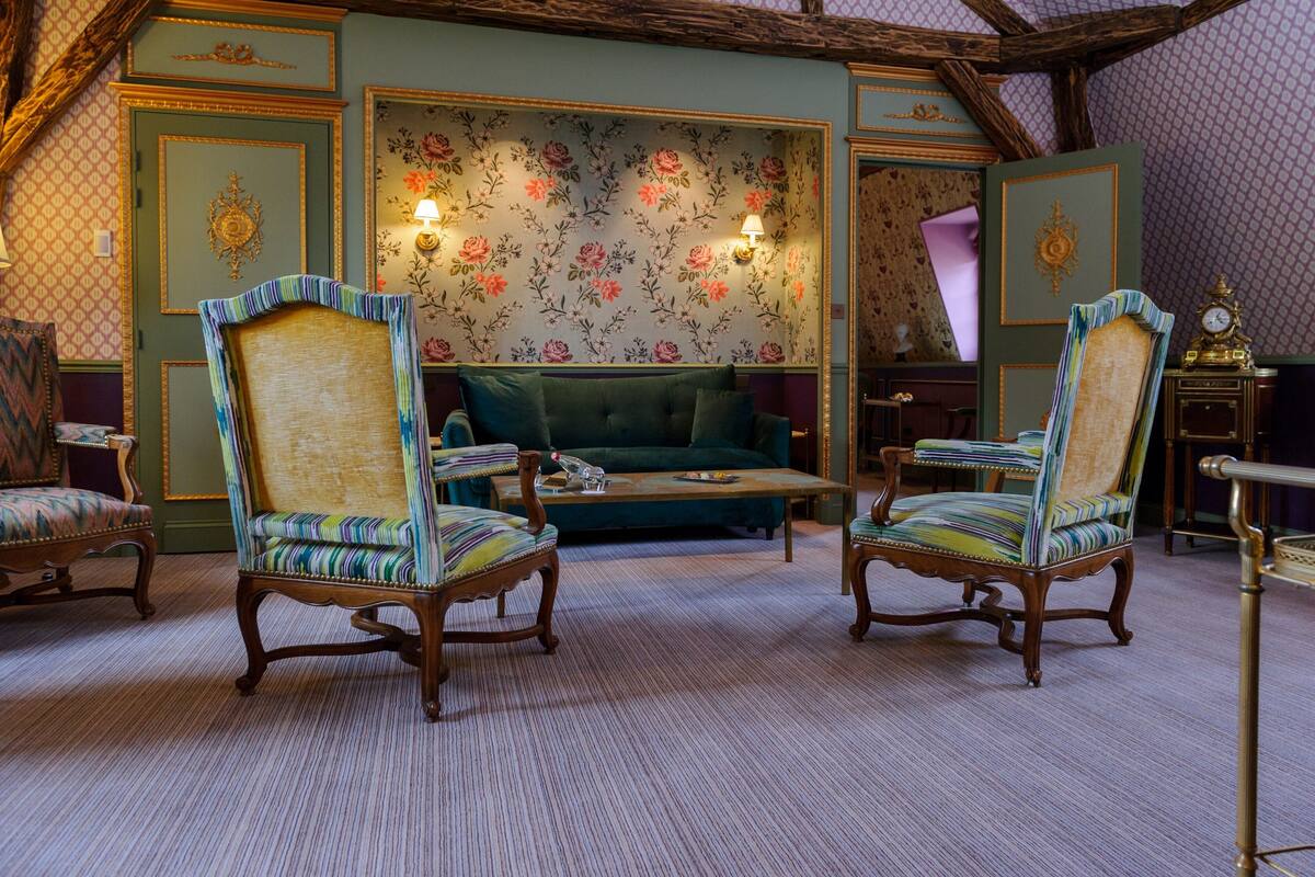 Une pièce comprenant deux fauteuils rembourrés, un canapé vert et une table basse en bois.