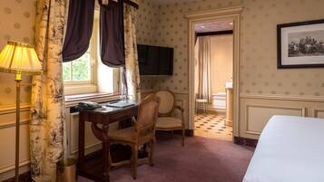 A hotel room with a desk, two chairs, a bed, a television, and a framed picture on the wall.