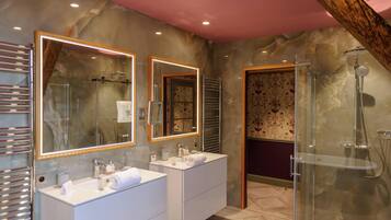 Un baño moderno con dos lavamanos, cabina de ducha de vidrio y paredes de mármol.