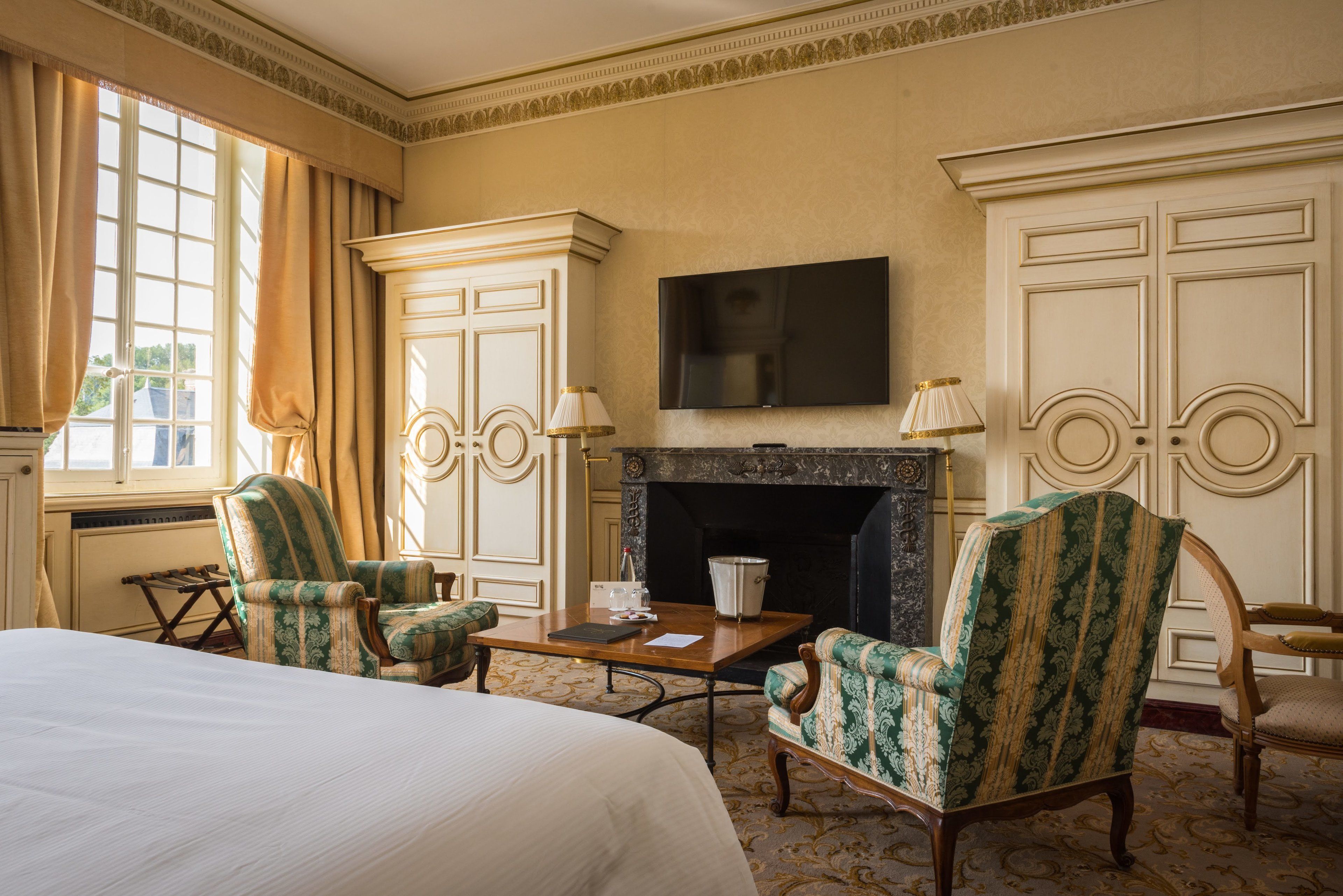Habitación de hotel con una cama grande, dos sillones, una mesita, chimenea y televisor montado en la pared.