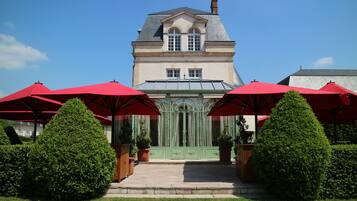 Un bâtiment à la façade symétrique, avec une entrée centrale dotée d’une porte verte et des parasols rouges devant.