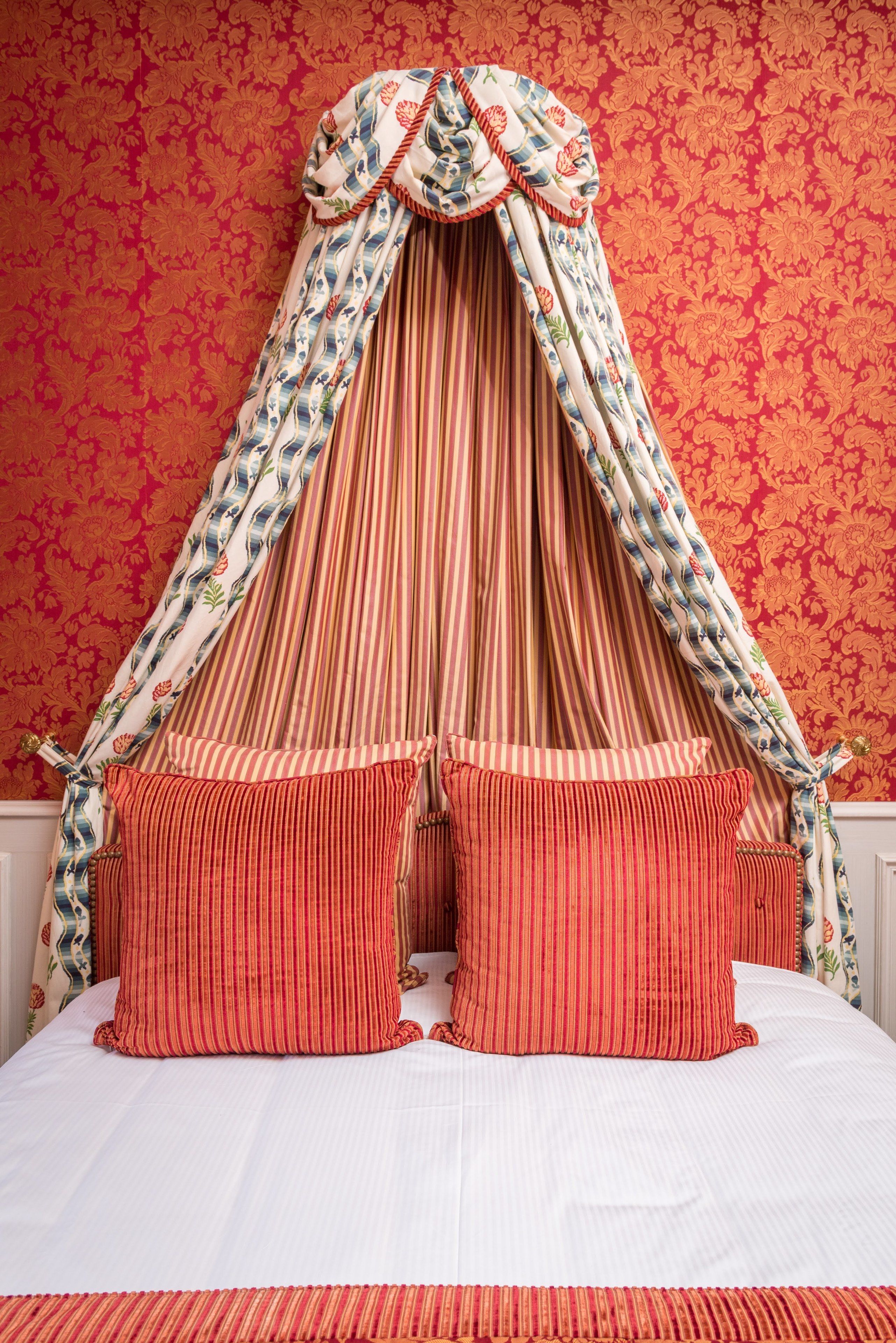 Una cama con dosel y almohadas a rayas sobre un papel tapiz floral.