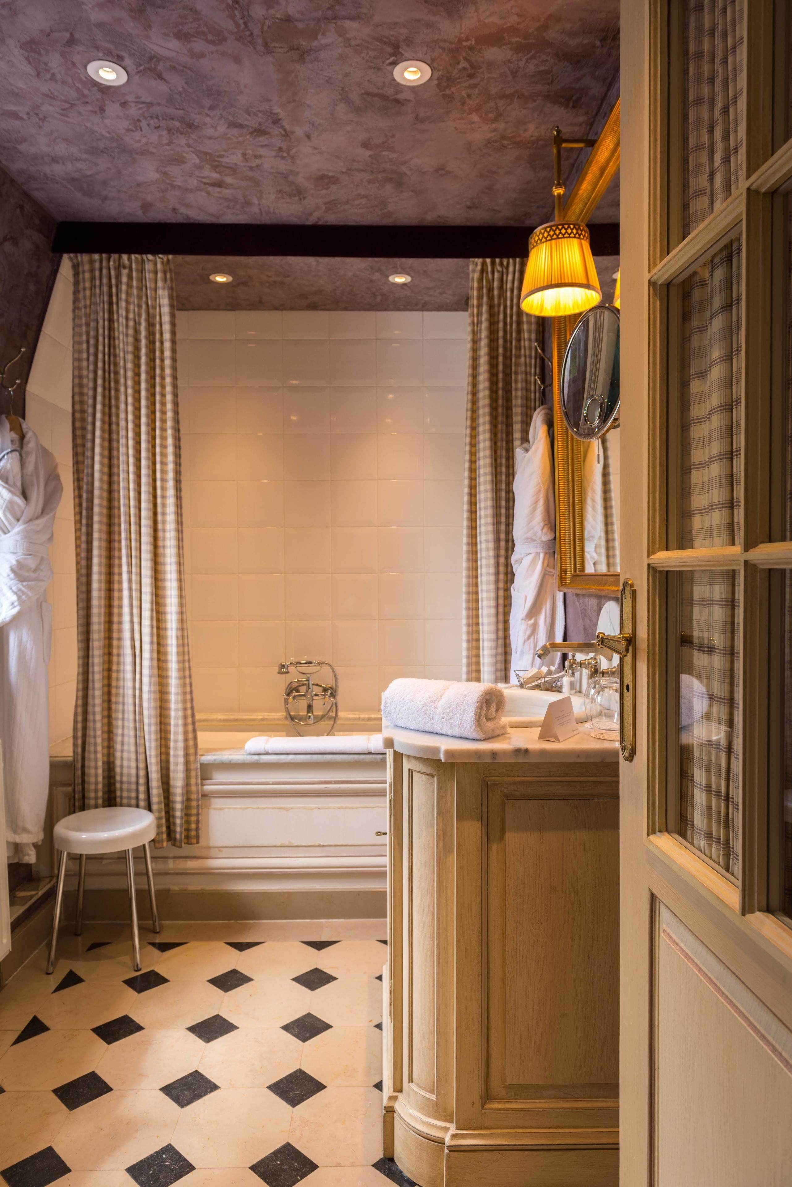 A bathroom with a bathtub, a sink with a mirror, and a stool.