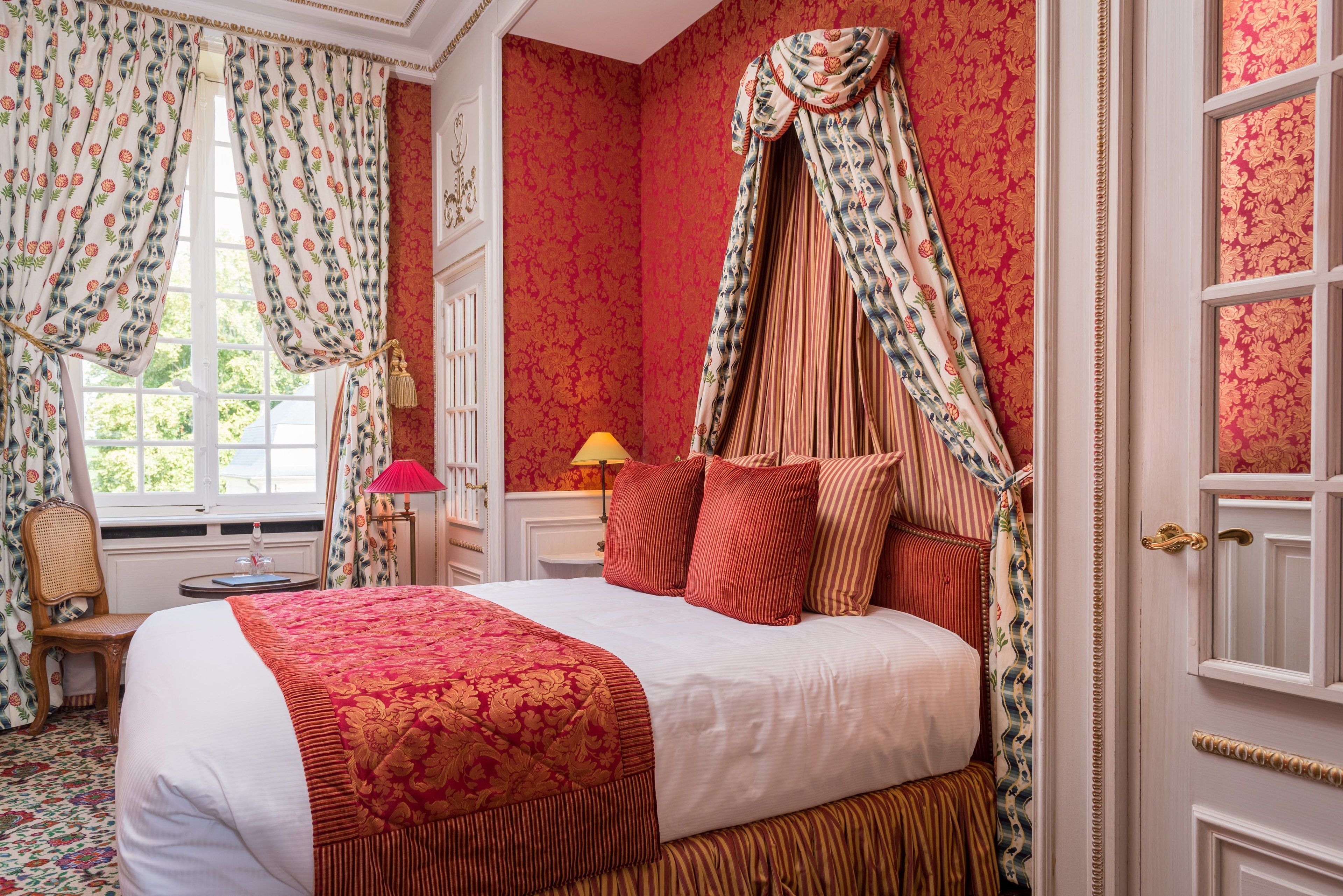 Un dormitorio con cama con dosel, papel tapiz floral y ventana con cortinas.