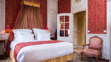 A bedroom with a four-poster bed, a red and white patterned bedspread, a red lamp, and a wooden chair.