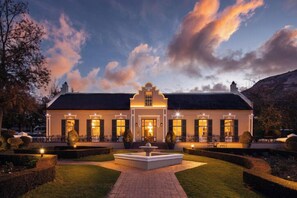 A large, well-lit building with a central entrance, surrounded by a manicured garden and a fountain. - Grande Roche Hotel (Paarl)