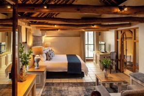 A cozy bedroom with a large bed, bedside tables, a desk, and a chair. There is a television and a window with curtains. - Grande Roche Hotel (Paarl)