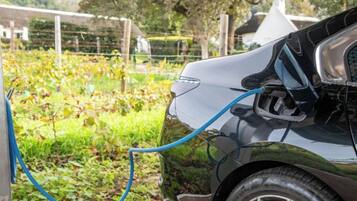 A parked electric vehicle charging in a garden area.