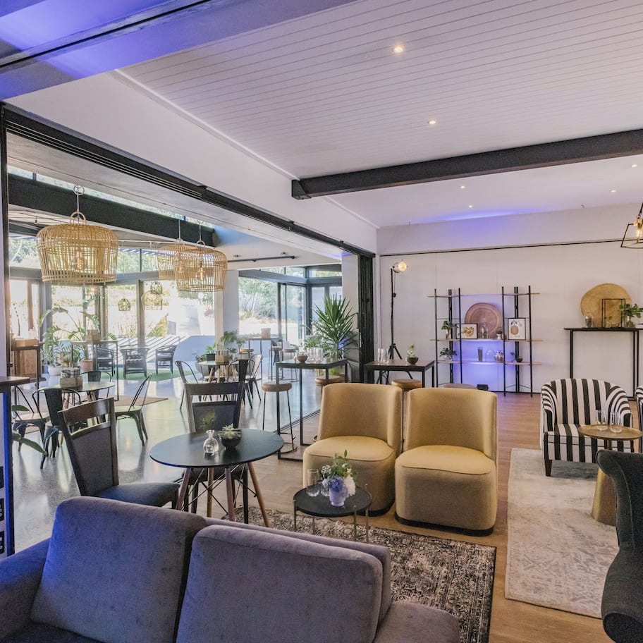 A modern living room with a sofa, armchairs, and a coffee table. There is a dining area with chairs and a table, and a kitchen area with a stove and cabinets.