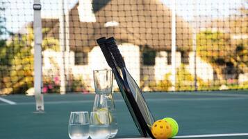 Una cancha de tenis con una red, una raqueta, un vaso de agua y un vaso de agua de limón, además de una pelota de tenis.
