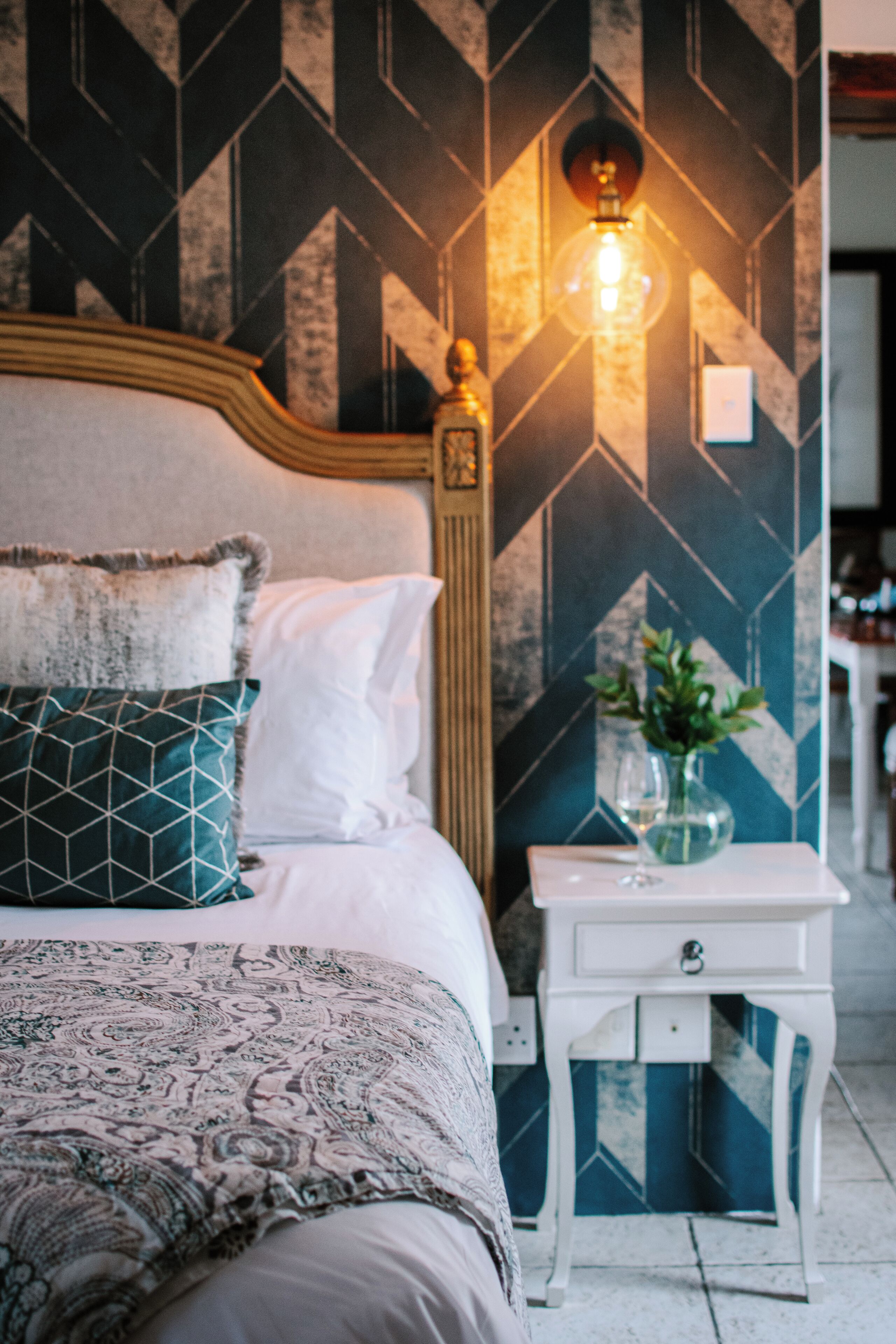 A bedroom with a bed, pillows, a nightstand, and a wall-mounted light fixture.