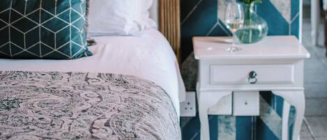 A bedroom with a bed, pillows, a nightstand, and a wall-mounted light fixture.