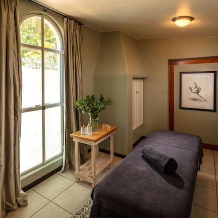 A room with a bed, a small table with a plant, a mirror, and a window with curtains.