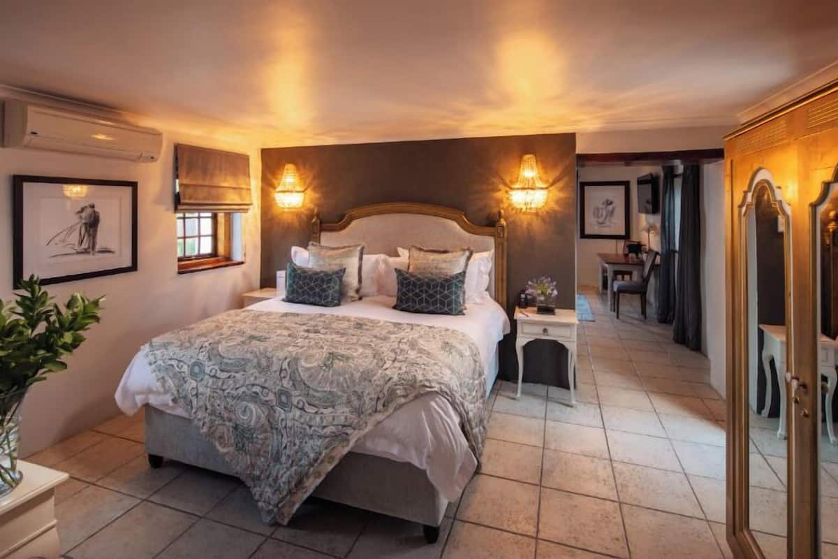 Une chambre à coucher avec un grand lit, deux lampes fixées au mur, un miroir et une petite table avec une lampe.