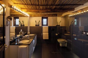A modern bathroom with a large mirror, dual sinks, a toilet, and a glass-enclosed shower.