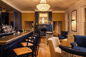 A bar area with a long counter, multiple bar stools, and a chandelier.