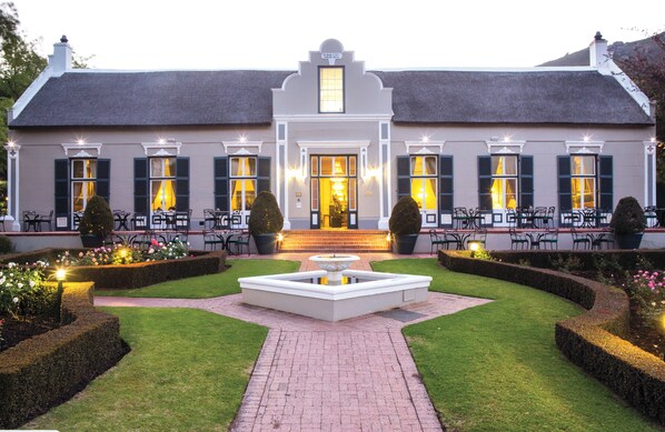 A stately building with a symmetrical facade, a central entrance, and a well-manicured garden with a fountain. - Grande Roche Hotel (Paarl)