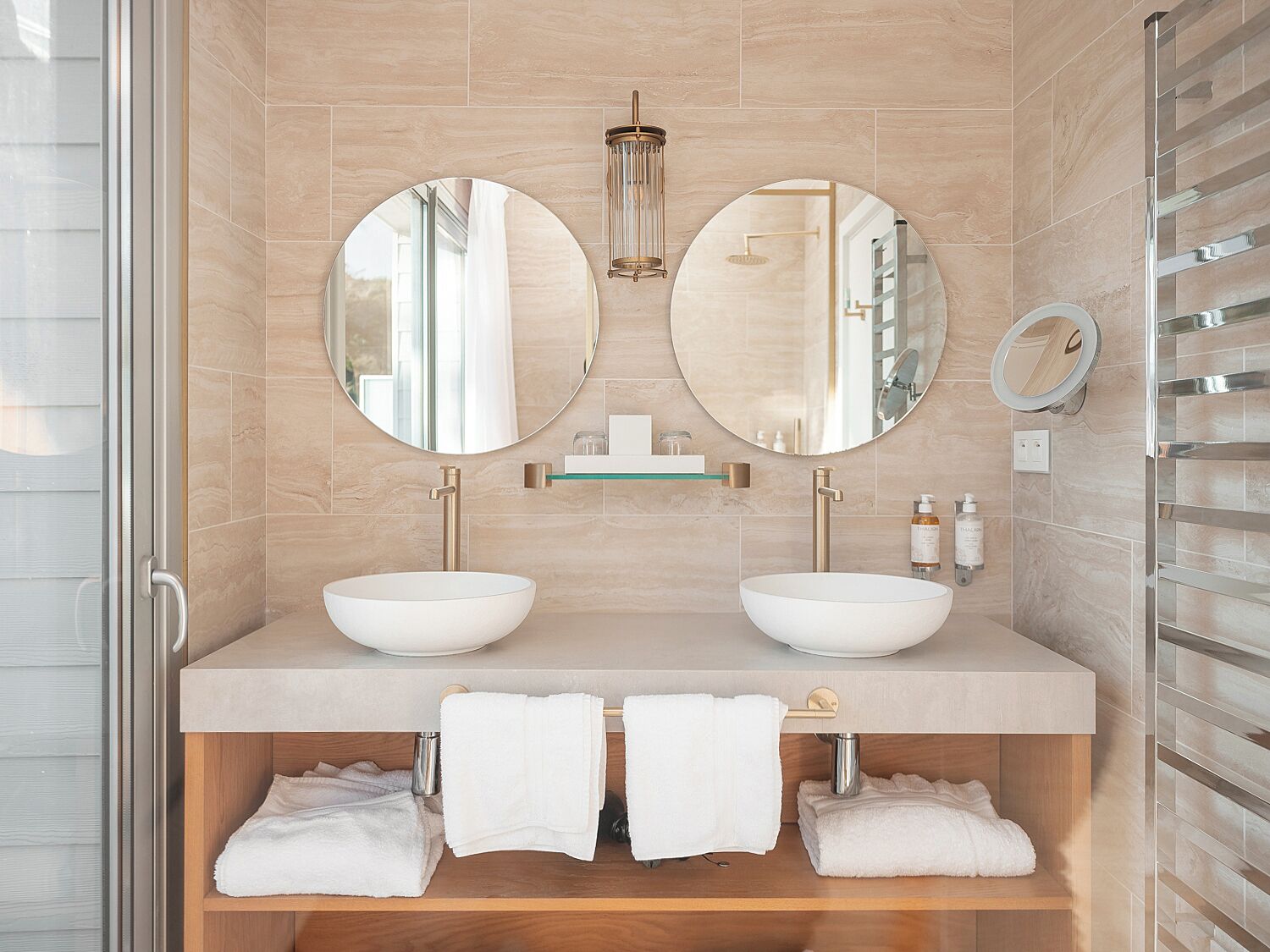 A modern bathroom with two sinks, a glass shelf, and a towel rack.