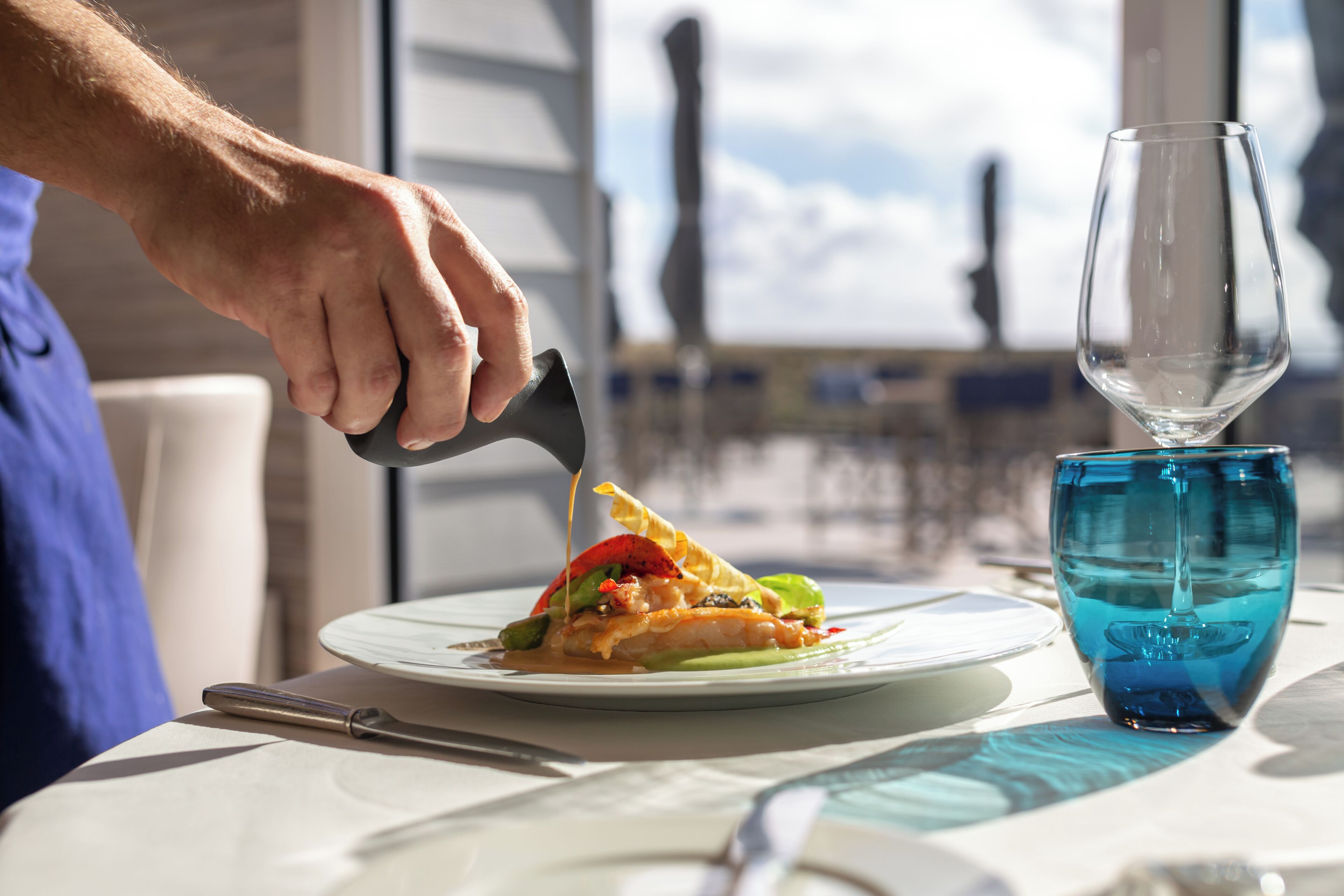 A person cutting a dish on a table with a blue glass and a knife.