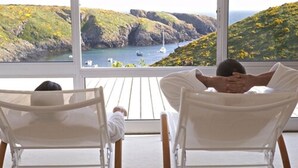 Two reclining chairs facing a scenic view of a coastal landscape with cliffs and boats. - Castel Clara Thalasso & Spa (Bangor)