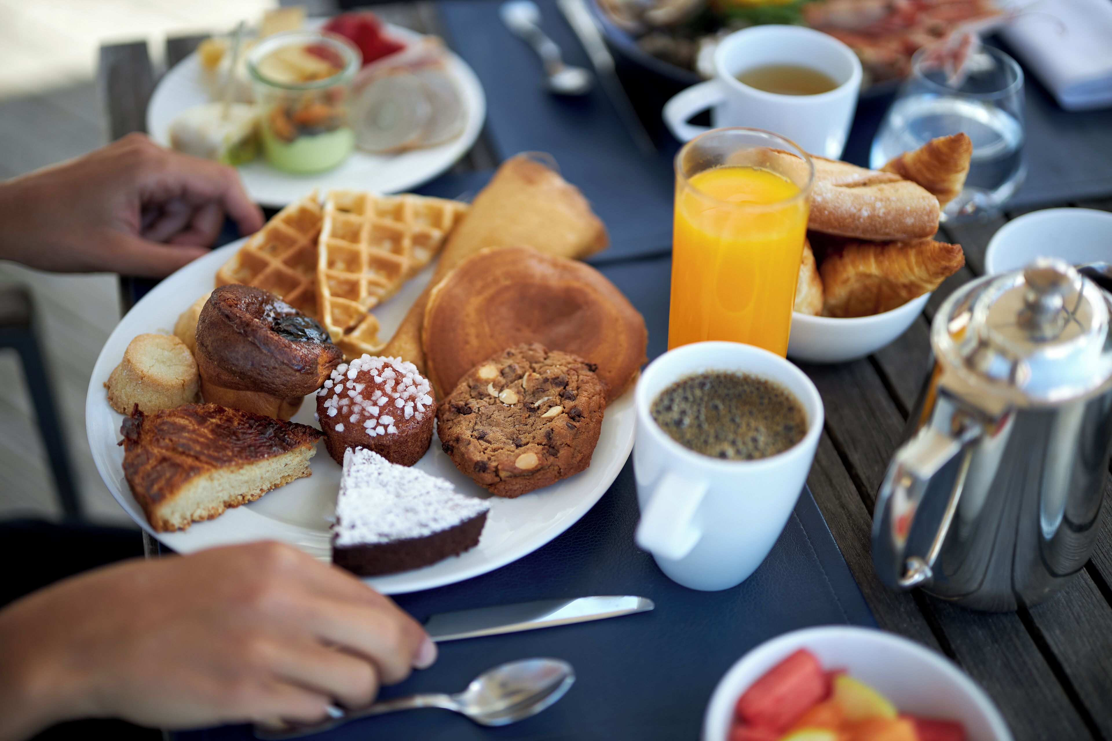 A breakfast table with various pastries, a waffle, a glass of orange juice, and a cup of coffee.