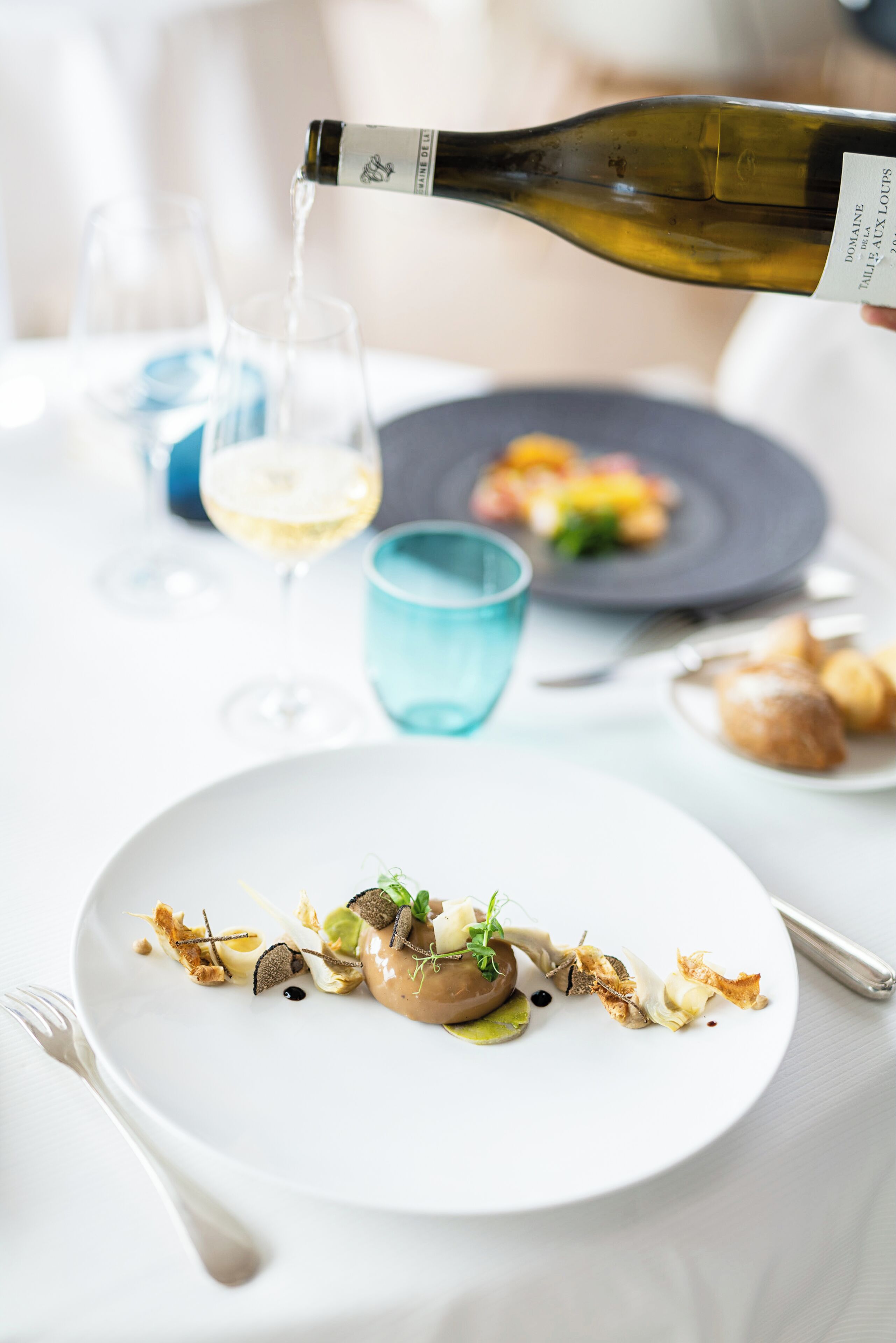 A dining table with a plate of food, a bottle of wine being poured, and glasses.
