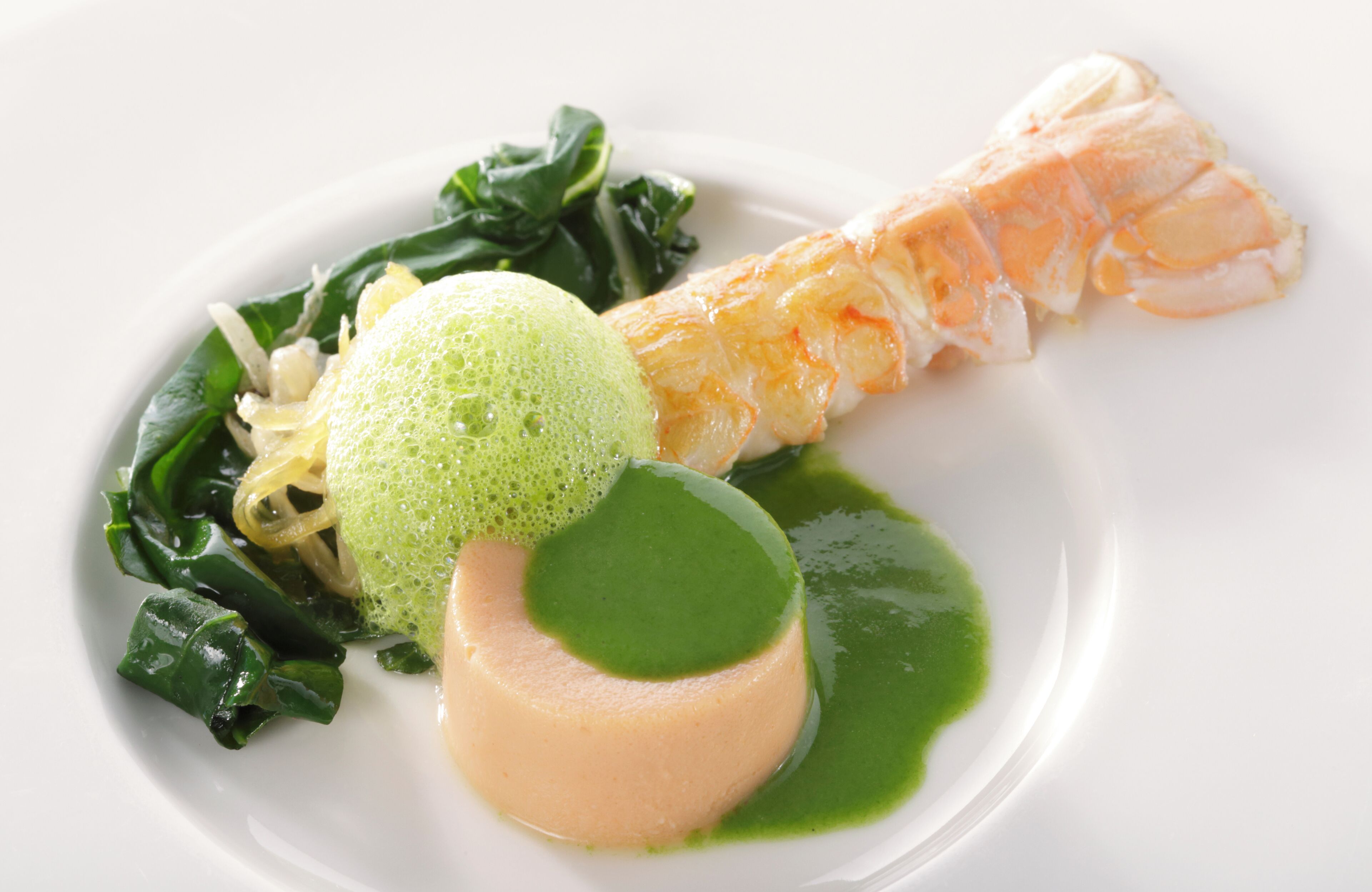 A plate with a fish, greens, and a green sphere.