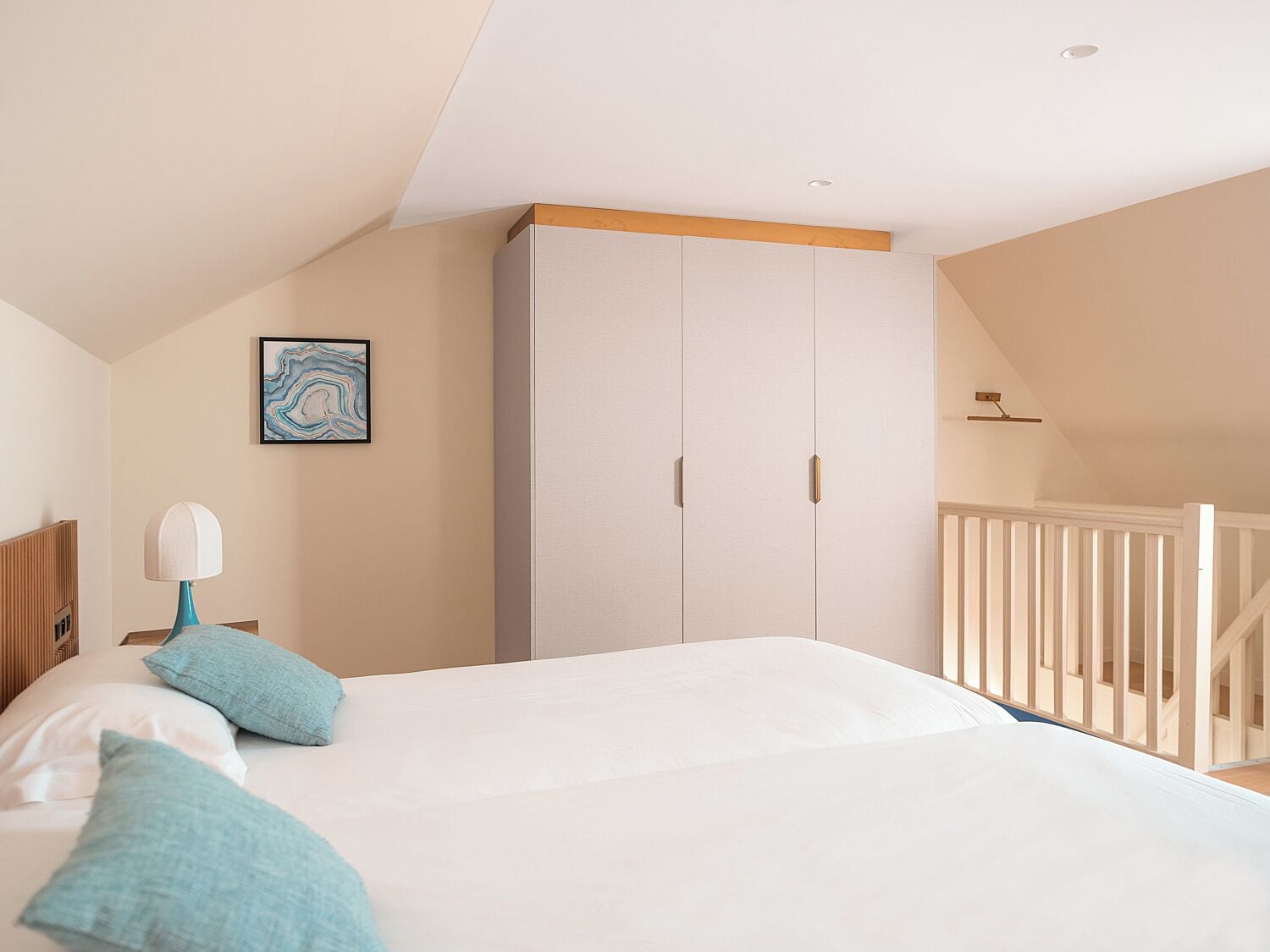 A bedroom with a large bed, a nightstand, a lamp, a framed picture, and a wardrobe.