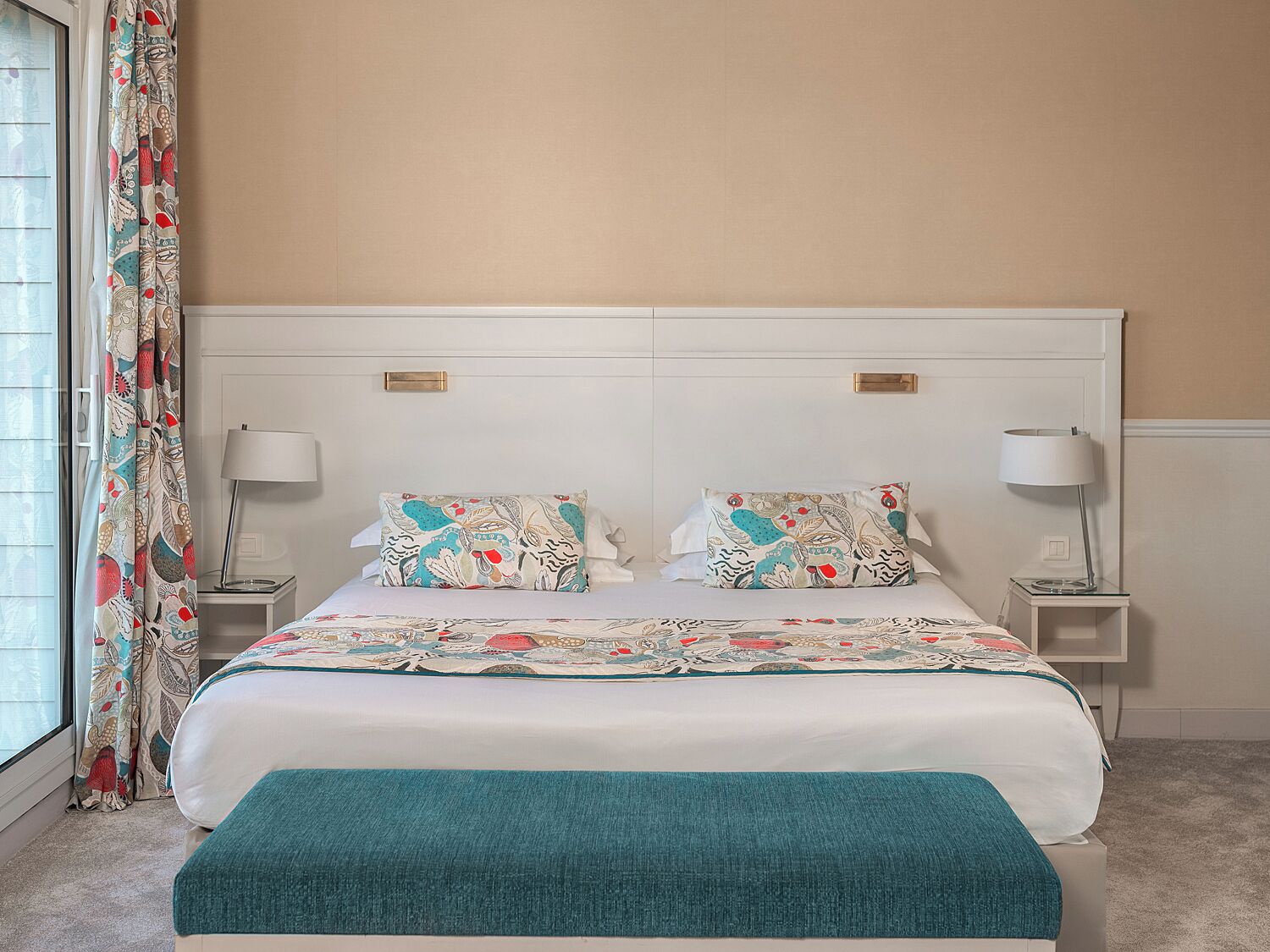 Une chambre bien rangée, avec un grand lit, deux tables de chevet dotées de lampes et une fenêtre avec des rideaux.