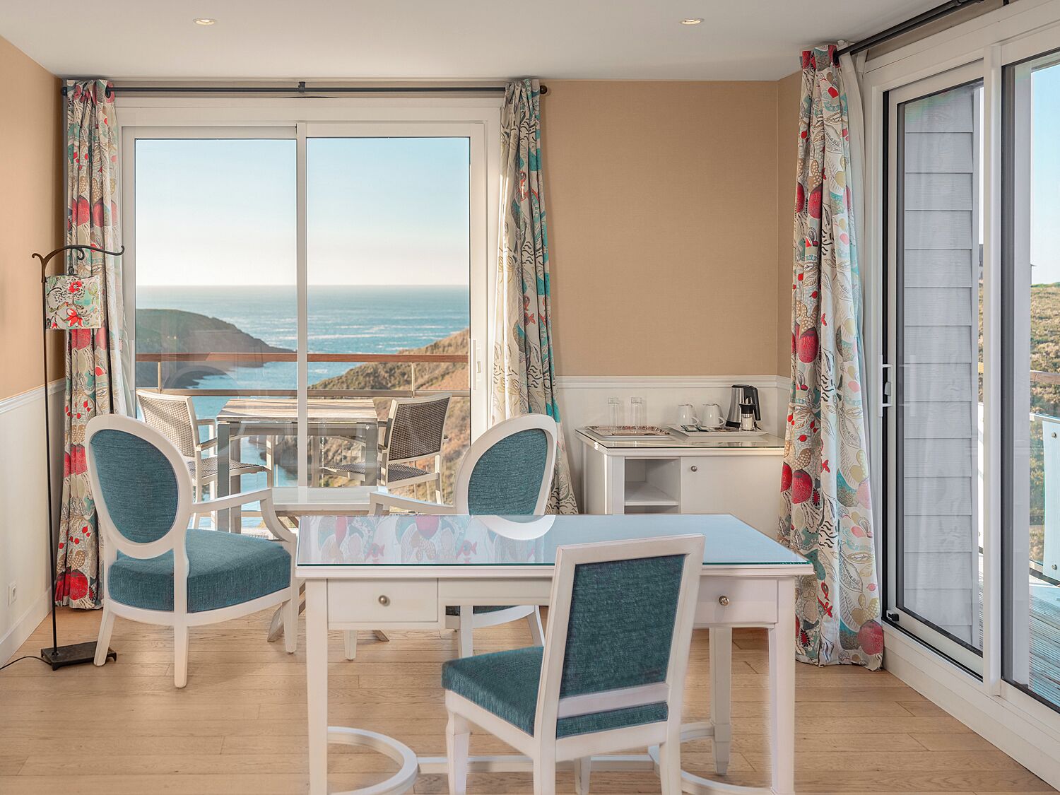 A balcony with a table and chairs, a small kitchenette, and a view of the ocean.