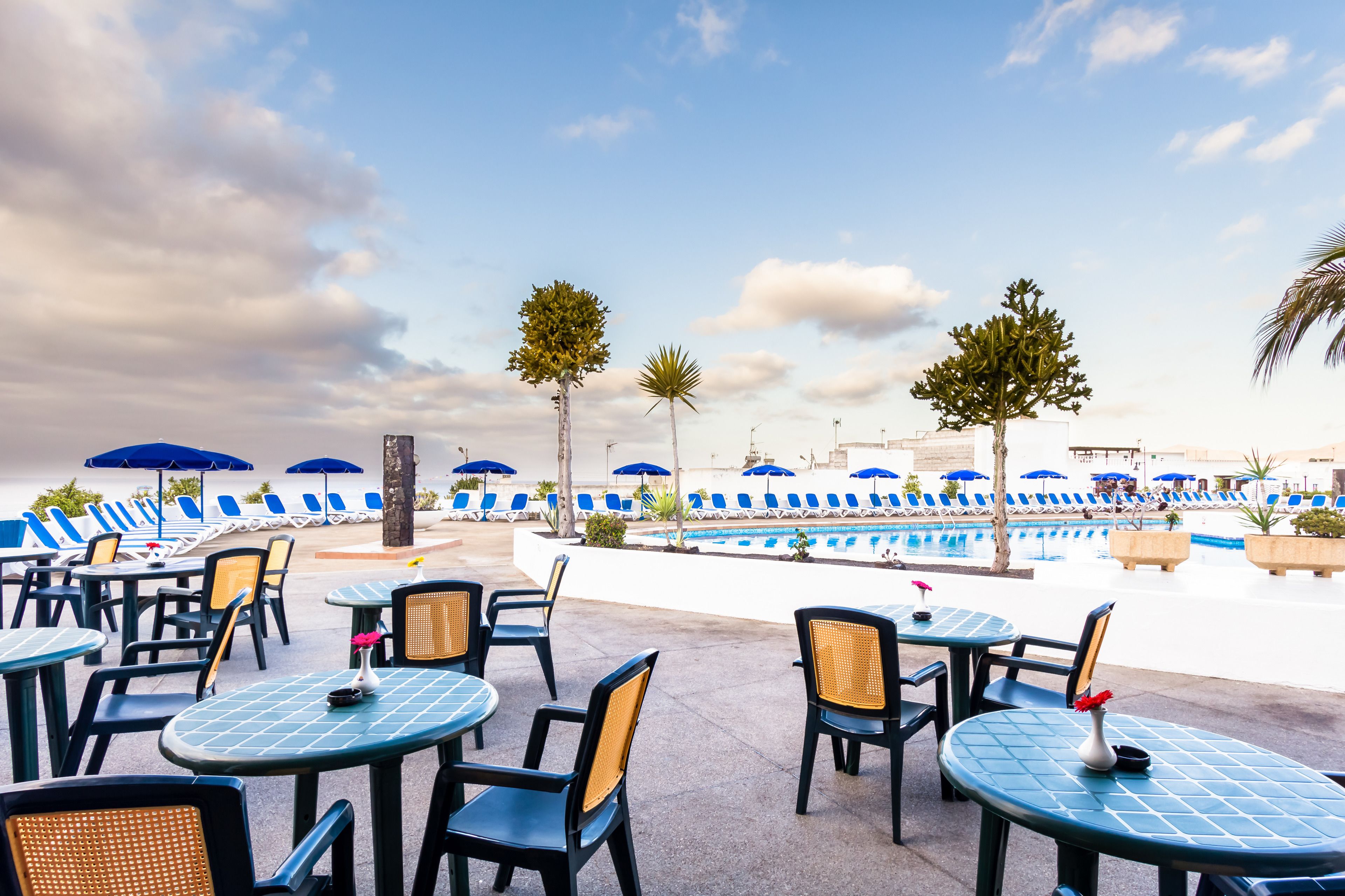 Een zwembadterras met ligbedden en parasols, tafels en stoelen voor gasten.