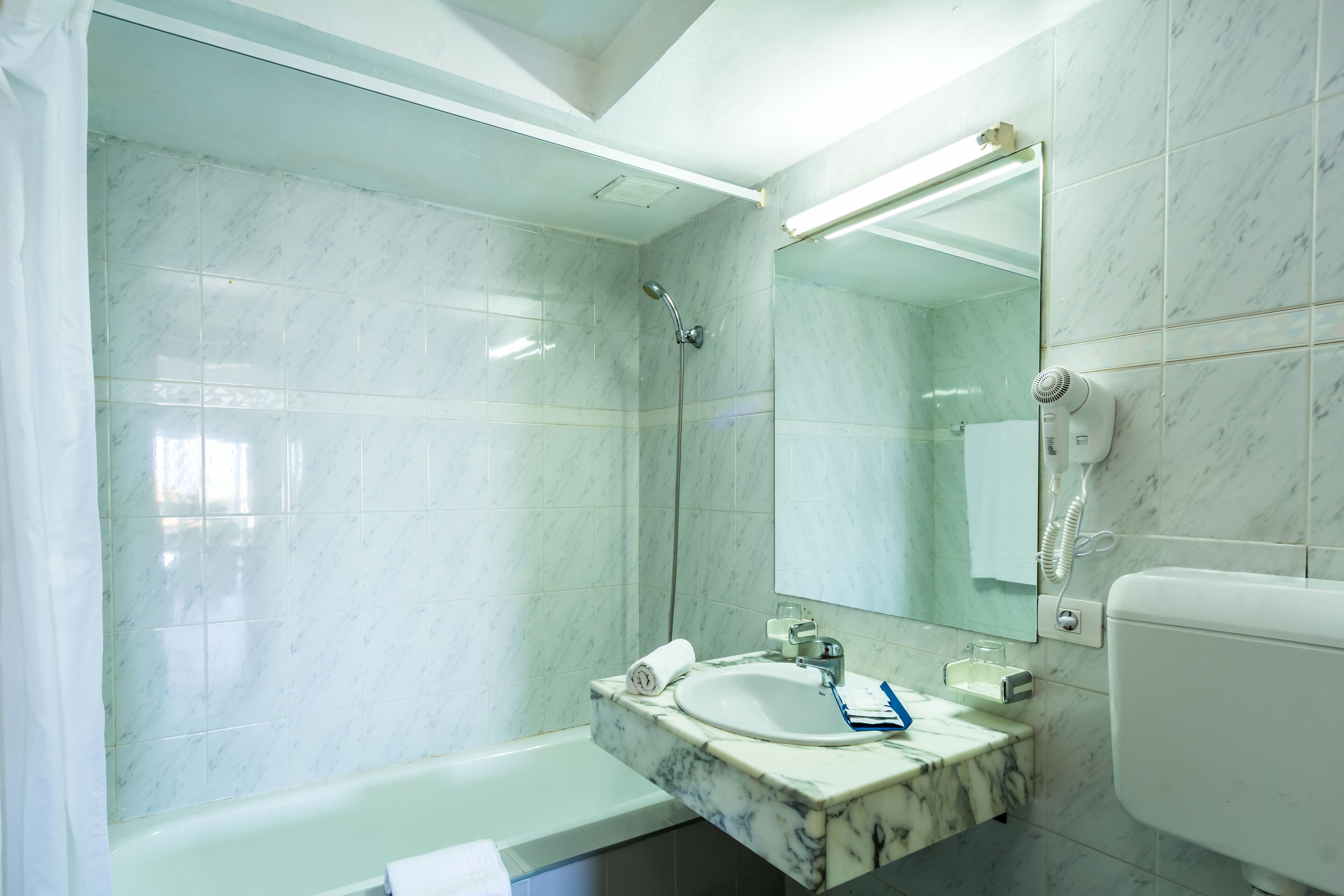 Een badkamer met een marmeren wastafel, een douche, toilet en een grote spiegel.