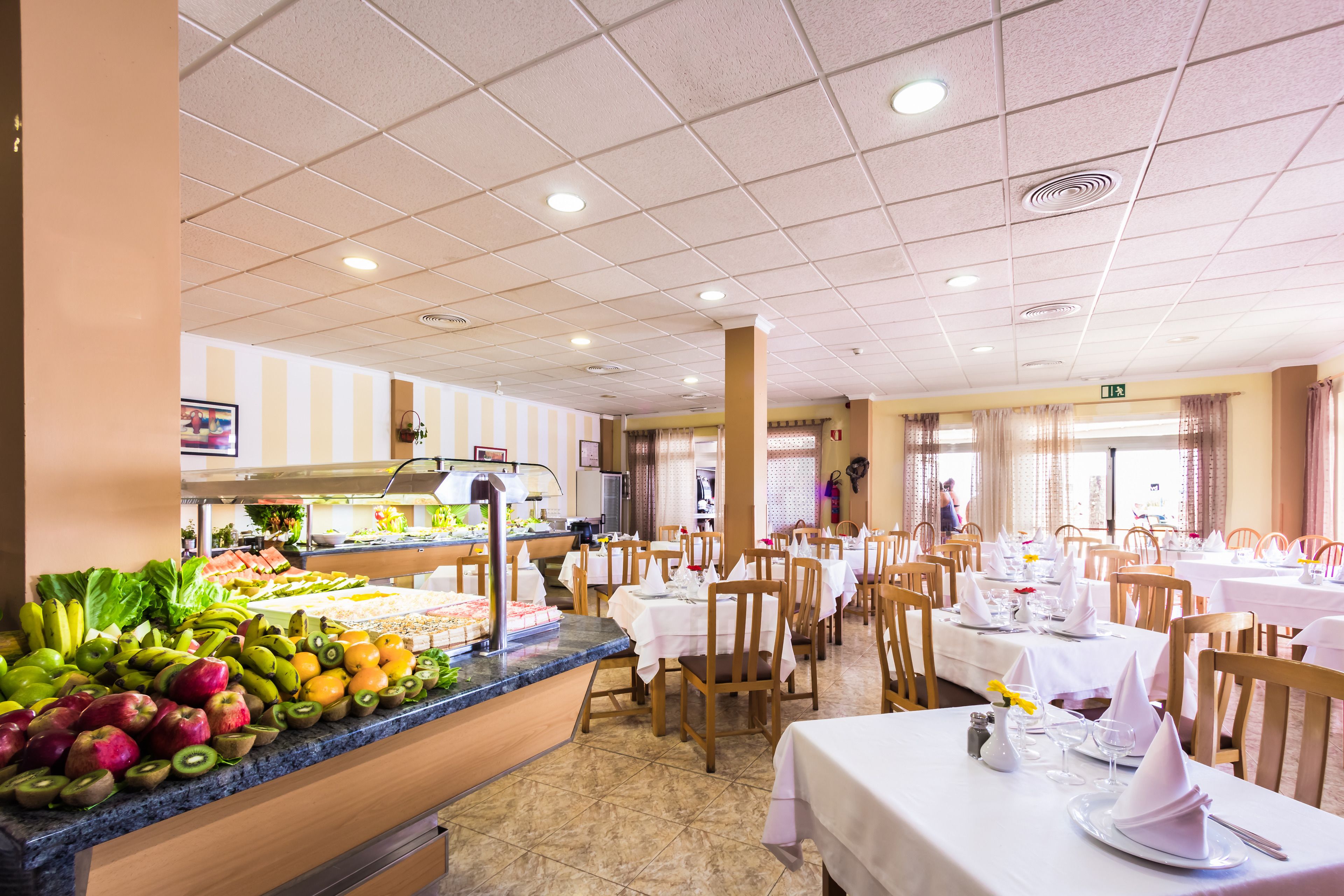 Un espace buffet proposant une variété de fruits et de légumes, des tables dressées pour le repas, et un sol carrelé propre.