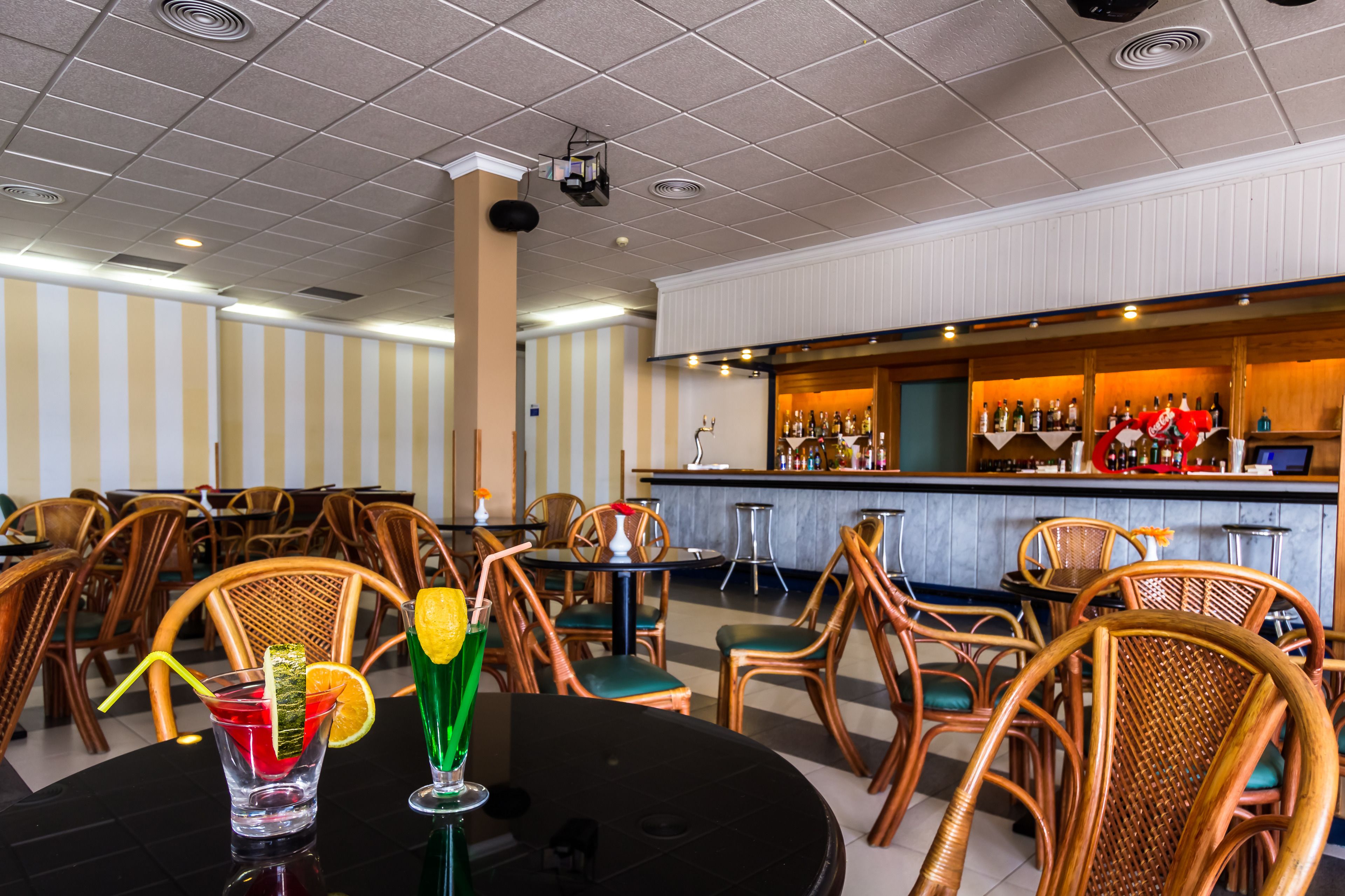A restaurant with striped walls, wooden chairs, and a bar area with bottles.
