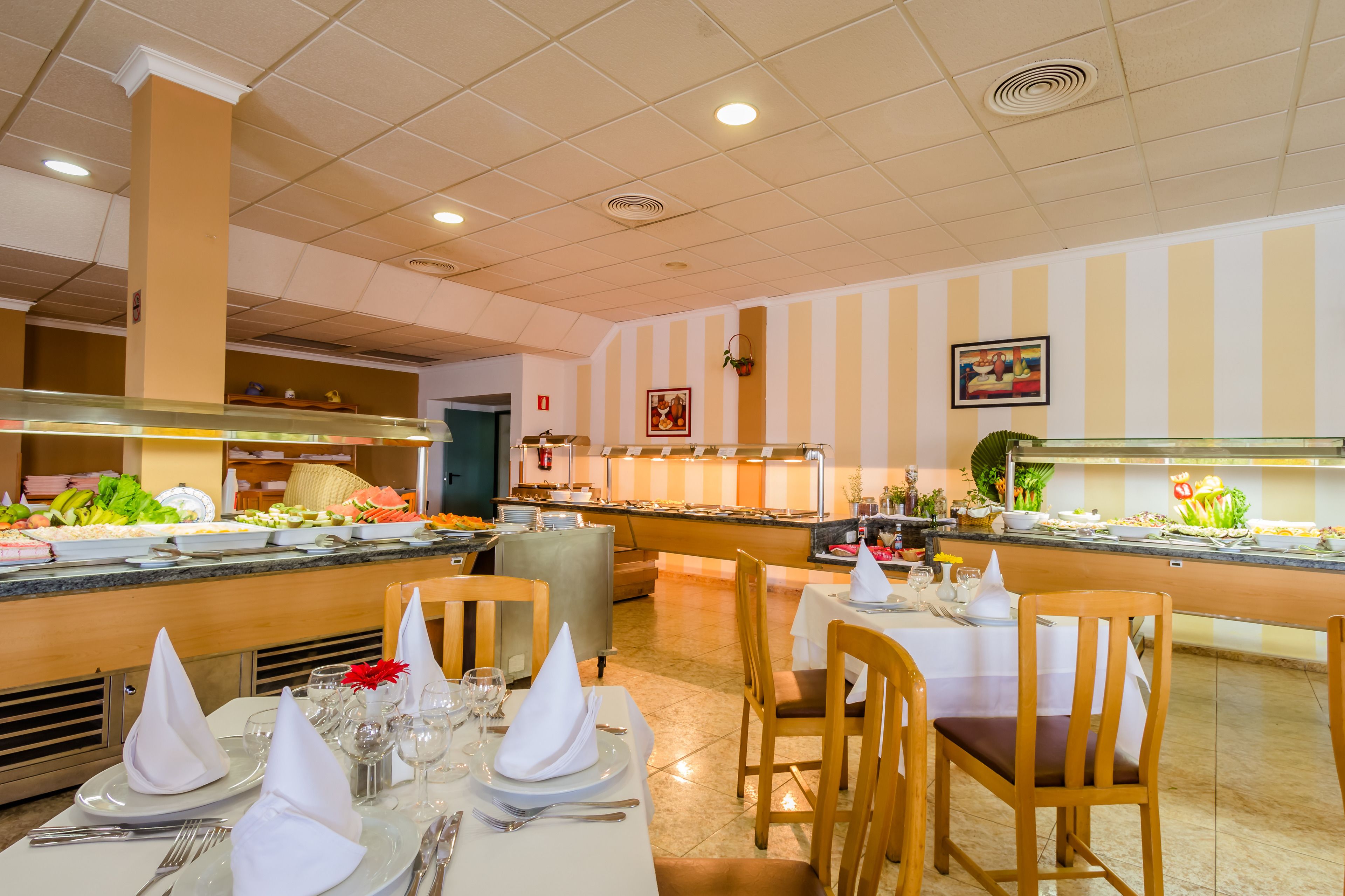 Een restaurant in buffetstijl met meerdere aaneenschakeling van bedieningspunten, een divers aanbod aan gerechten en netjes opgemaakte tafels met stoelen.