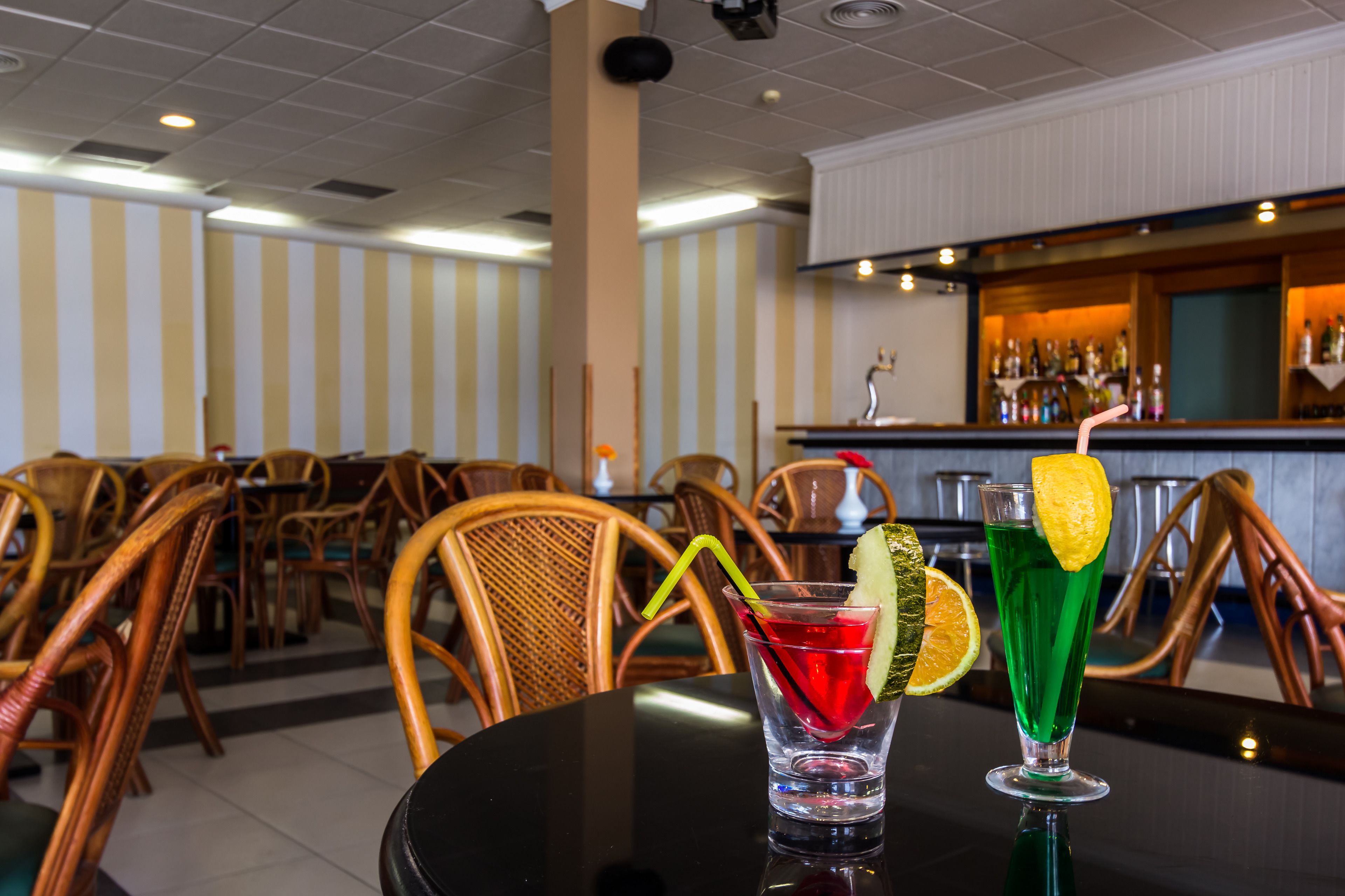 Un espace bar avec des murs à rayures, des chaises en bois et un comptoir où sont exposées des bouteilles.