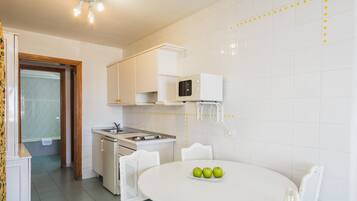 A small kitchen with white cabinets, a microwave, a sink, and a dining table with chairs. There are three apples on the table.