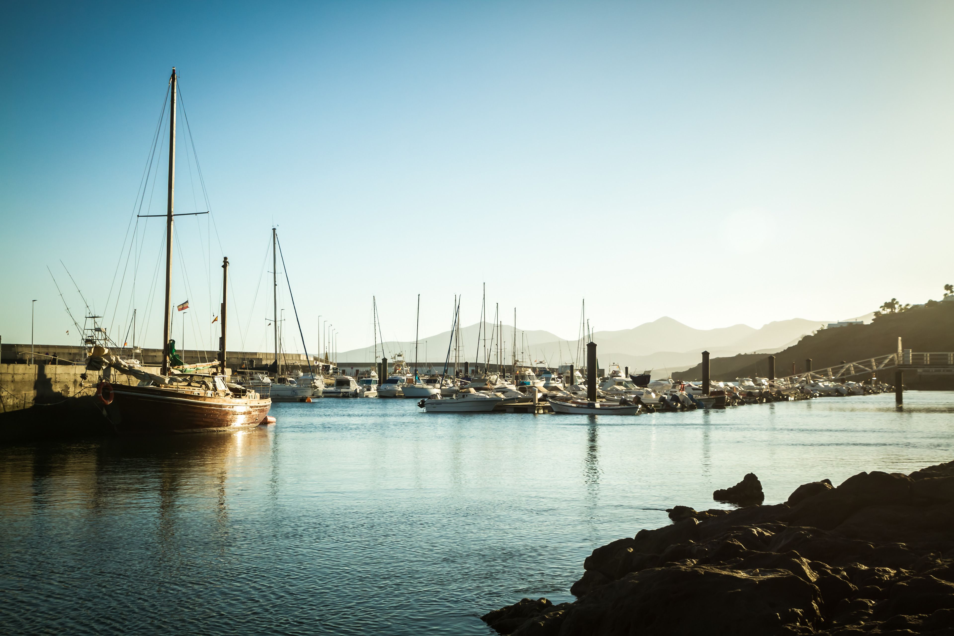 A marina with multiple boats docked, calm water, and a clear sky.