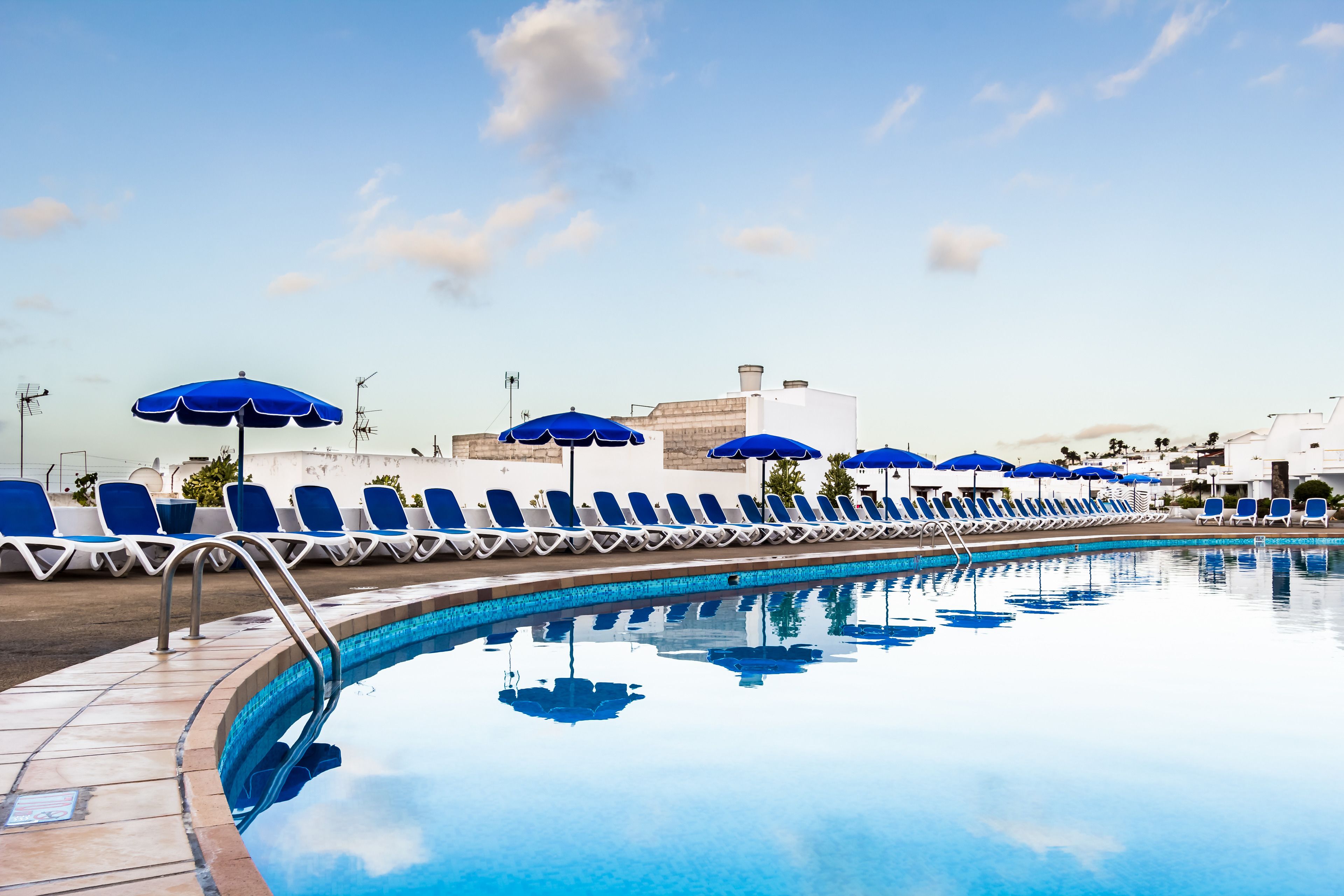 A swimming pool with blue chairs and umbrellas, surrounded by buildings.