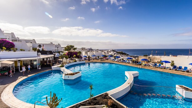 Una piscina grande y curvada con vista al mar y edificios blancos al fondo.