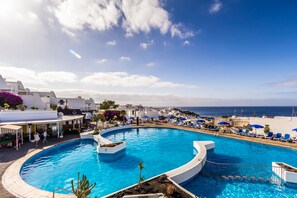 Una piscina grande y curvada con vista al mar y edificios blancos al fondo.