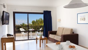 Une chambre d’hôtel avec un balcon, un canapé, une table avec des pâtisseries, une télévision et un tableau encadré au mur.
